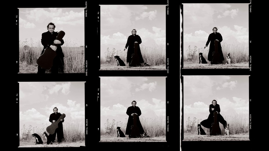 black and white contact sheet with 6 photos of Johnny Cash in long black coat with guitar case and dogs in a field