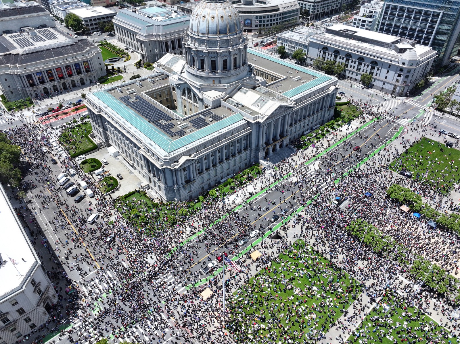 An overhead view of a large crowd of protesters gathered in squares and streets around a large city hall building.
