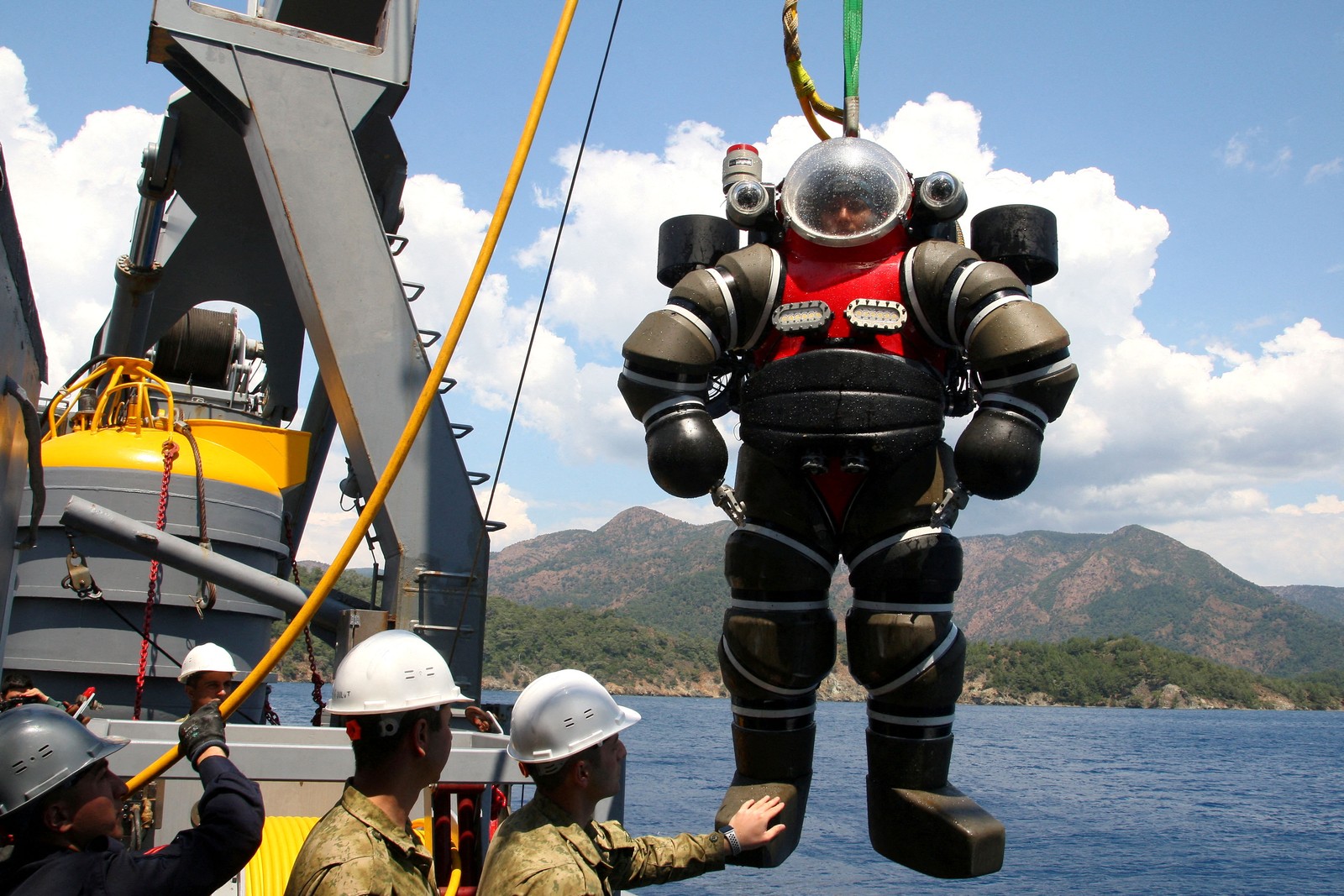 A diver wearing a heavy-duty armored diving suit is raised onto a ship from a dive.