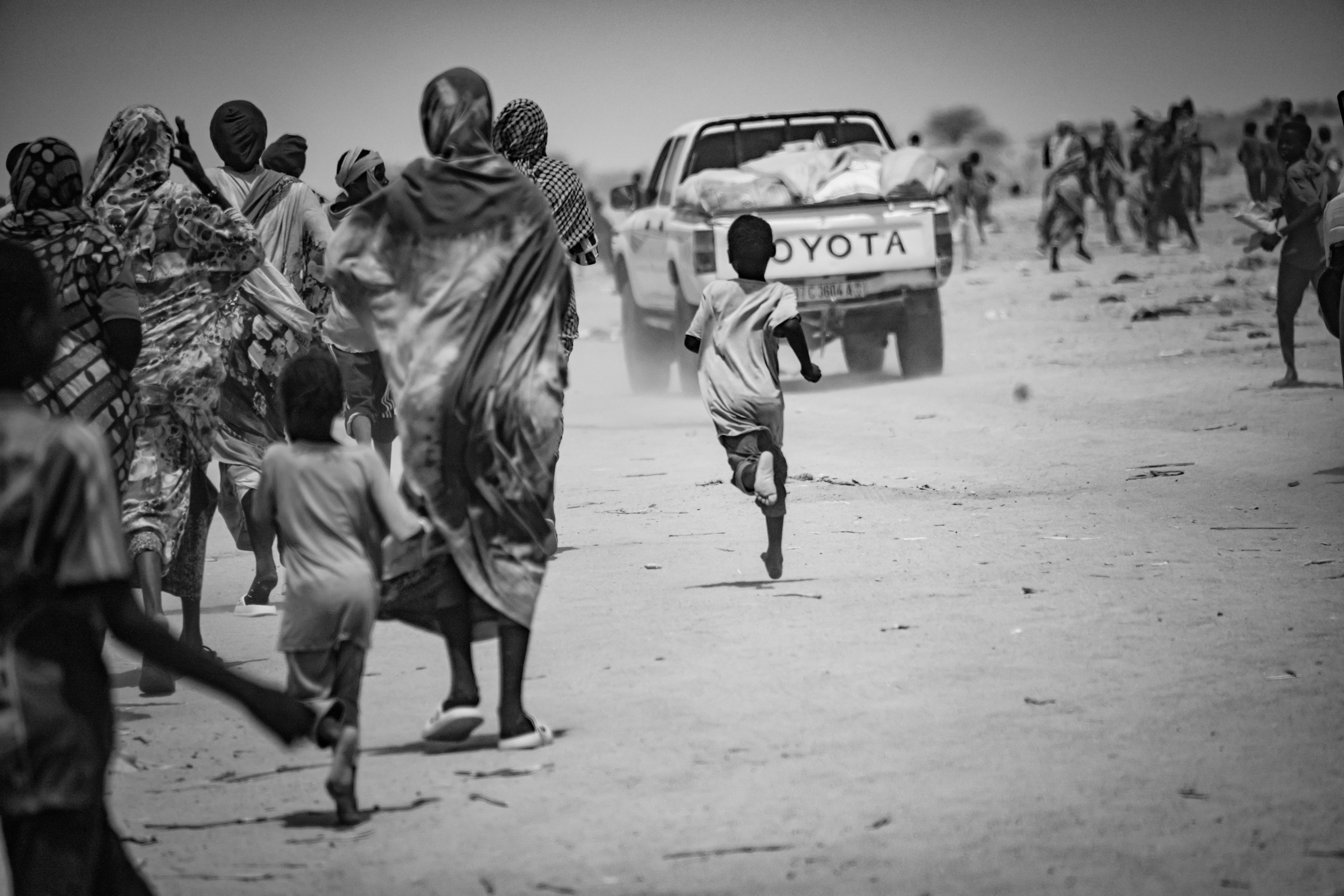 Picture of hungry Sudanese refugees running after trucks ferrying hot meals and food donated by the local community in Chad.