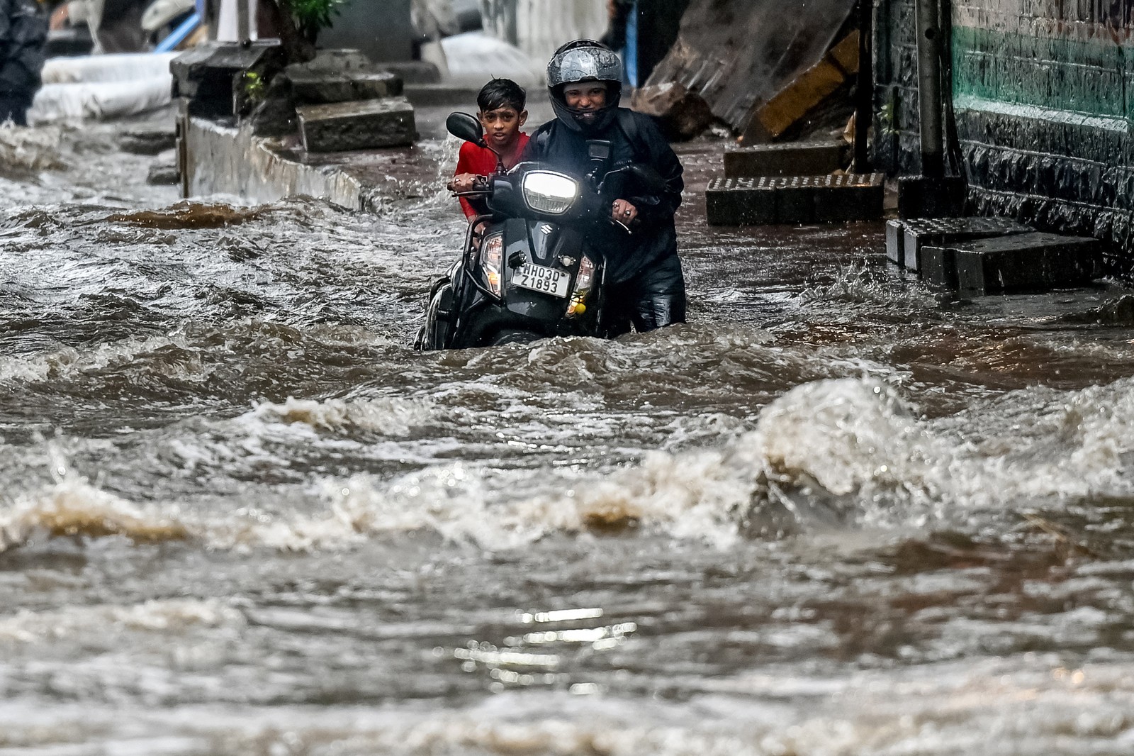 A person pushes a scooter through churning floodwater.