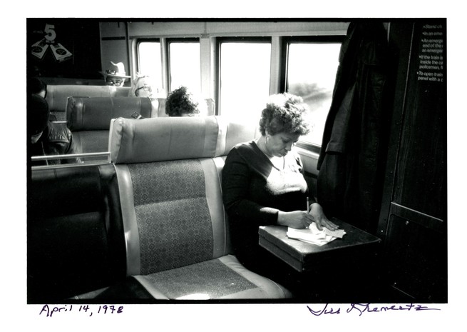a black and white photo of the novelist Toni Morrison sitting on a train and writing on a stack of papers