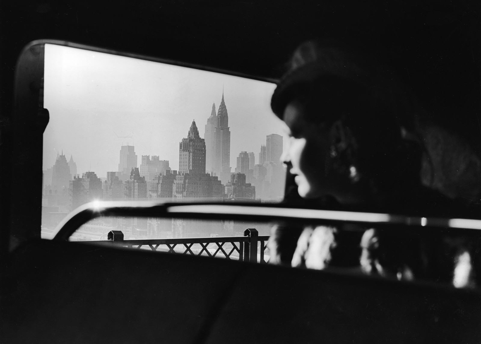 A passenger on bus looks out a window toward a hazy New York City midtown skyline.