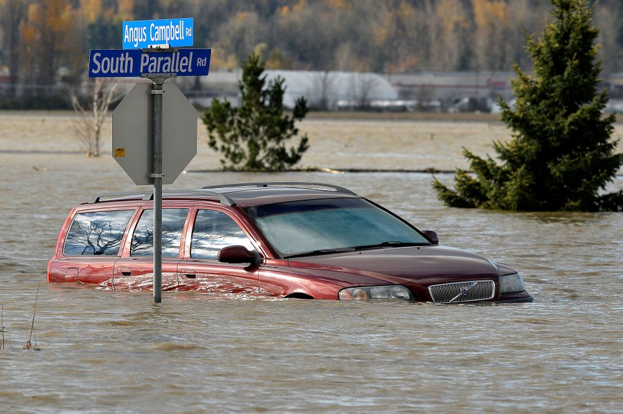 A station wagon sits half-submerged in floodwater, near a street sign.