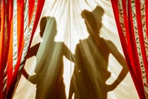 The silhouettes of a woman and a child behind red-and-gold-striped curtains