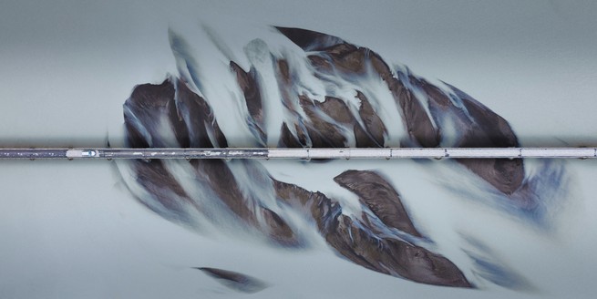 Iceland from above, with a bridge extending from left to right while abstract shapes emerge from flowing river water originating from a glacier