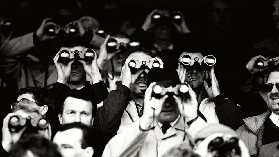 A black-and-white photograph of several men holding binoculars up to their faces to look at something far away