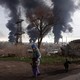 A woman walks in Odesa, Ukraine, as three large columns of smoke billow in the distance.