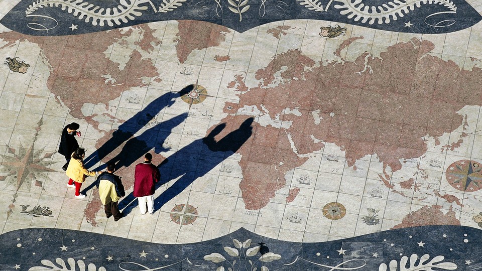 Four people stand on top of a large world map.