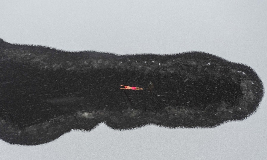 An aerial view of a person swimming in in a partially-frozen lake.