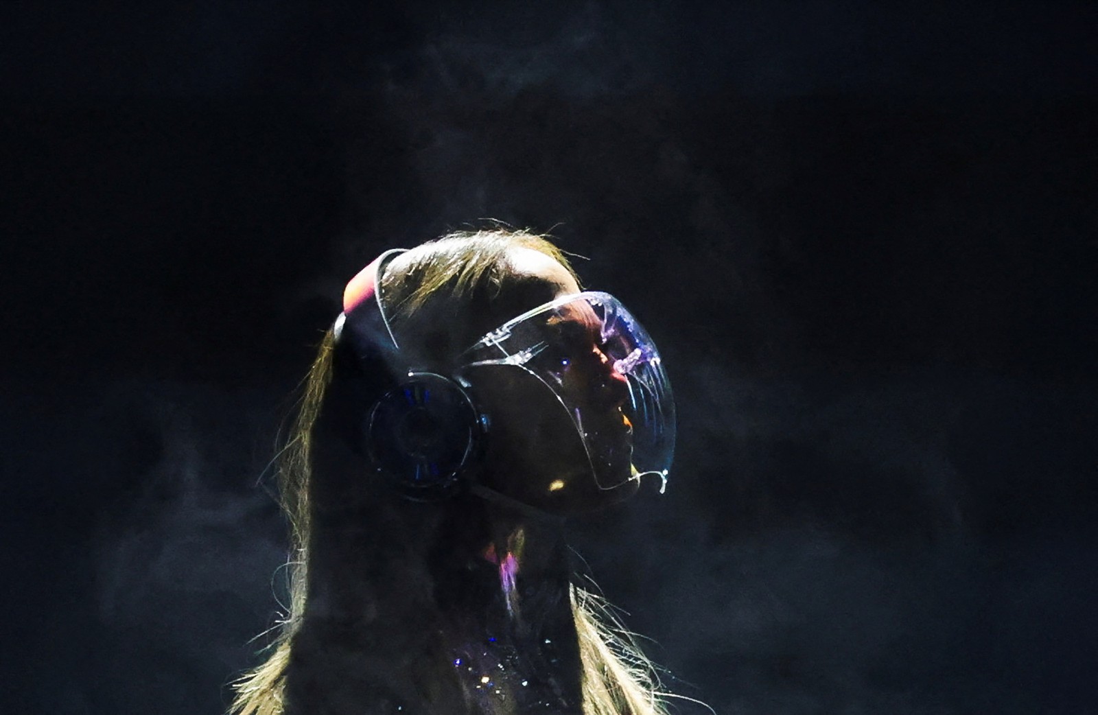 A profile view of Jennifer Lopez, wearing a curved clear, face shield, while performing on stage