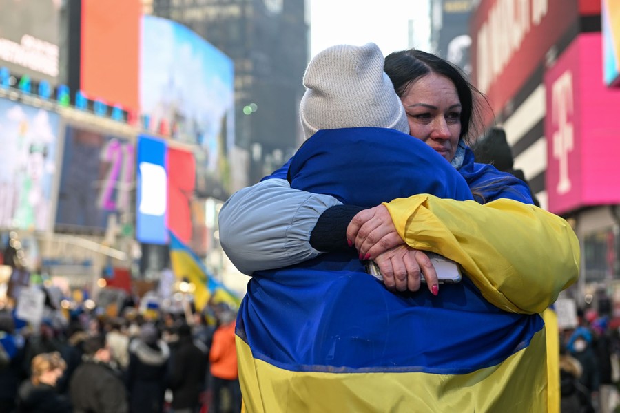 Two people draped in Ukrainian flags embrace during a protest.