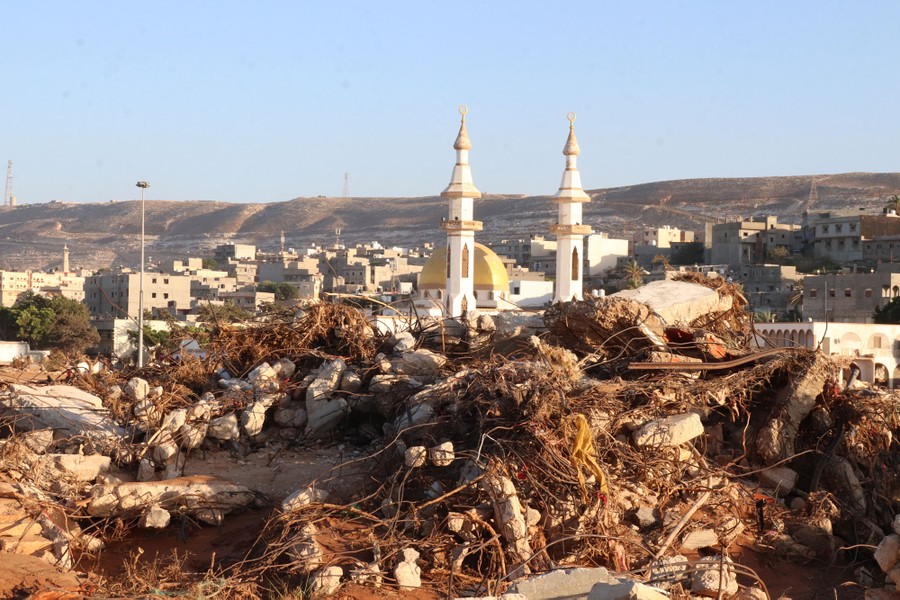 A pair of minarets stand in the background, behind a large pile of flood debris.