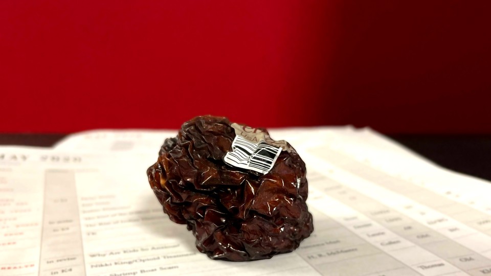 A shrunken, shriveled apple on top of a pile of papers against a red backdrop