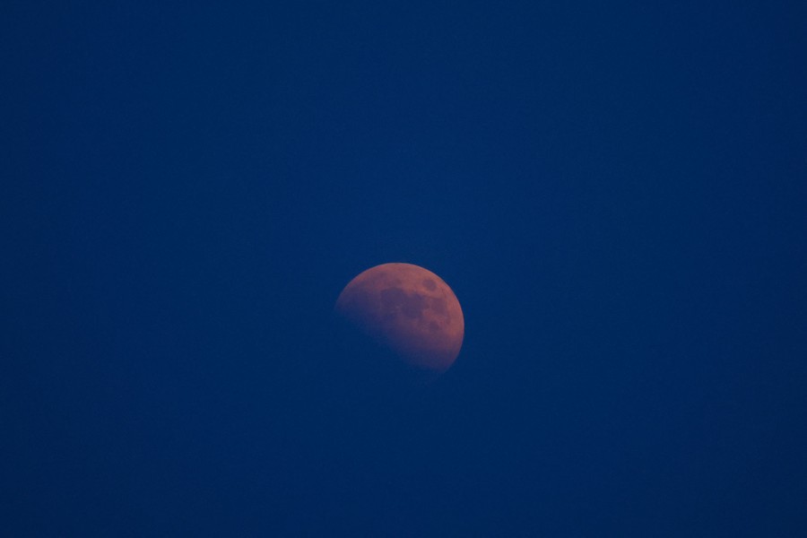A reddish half-lit moon appears in a dark-blue sky.