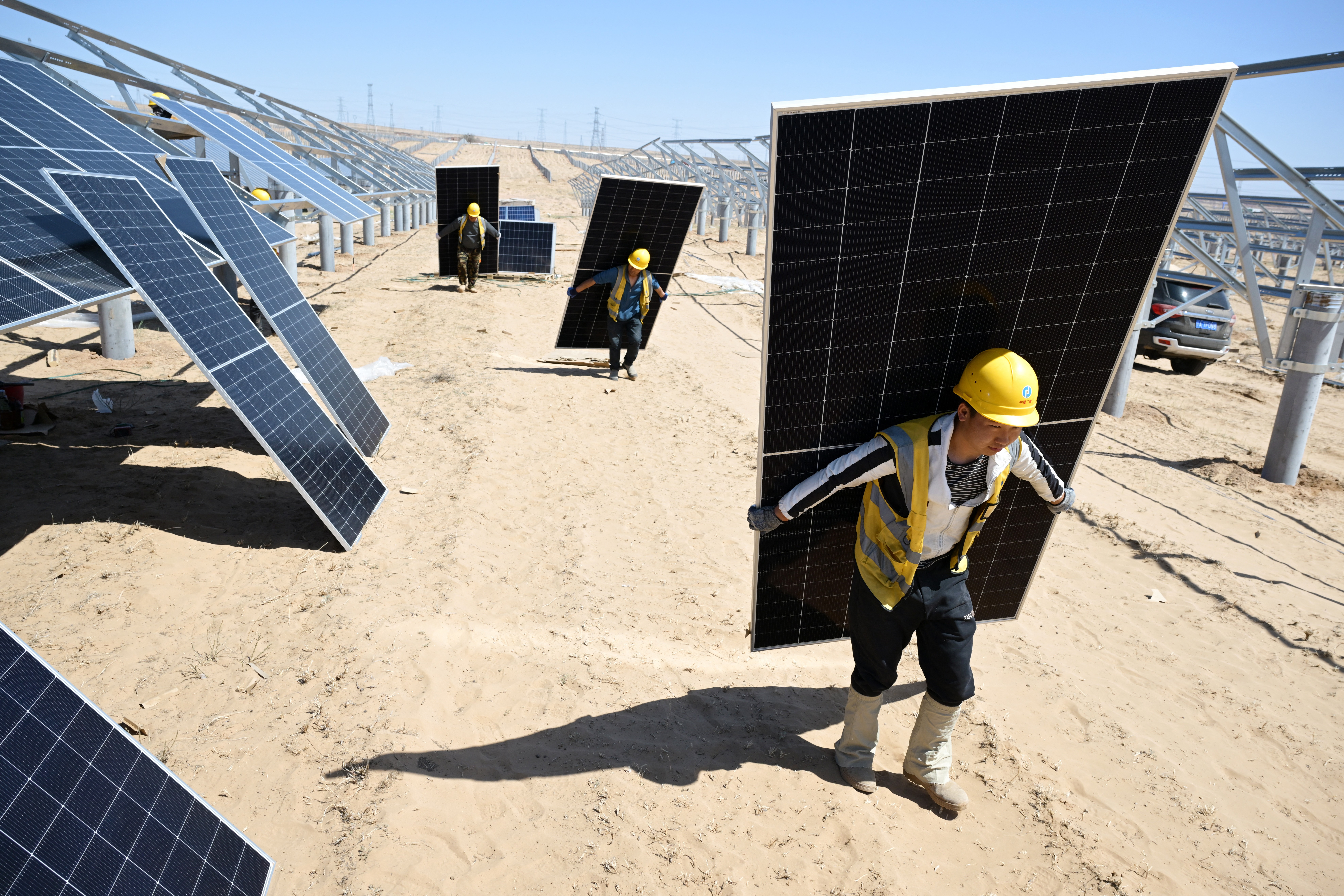 Three workers carry solar panels in a desert construction site.