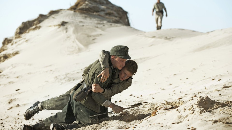 One German trooper, Anders, helps his fellow soldier, Hans, across the dunes in the Danish film, Land of Mine.