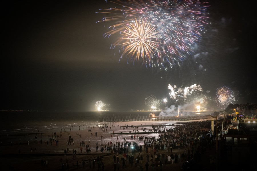 A crowd gathers on a beach, watching a fireworks display.