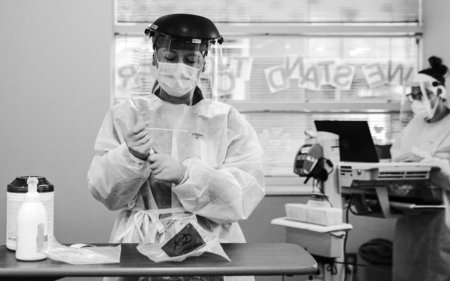 A black-and-white photo shows a nurse holding a swab taken from a patient for testing at the University of Iowa Hospitals and Clinics