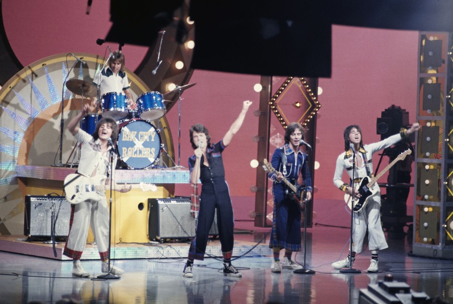Five members of a pop band perform in a television studio.