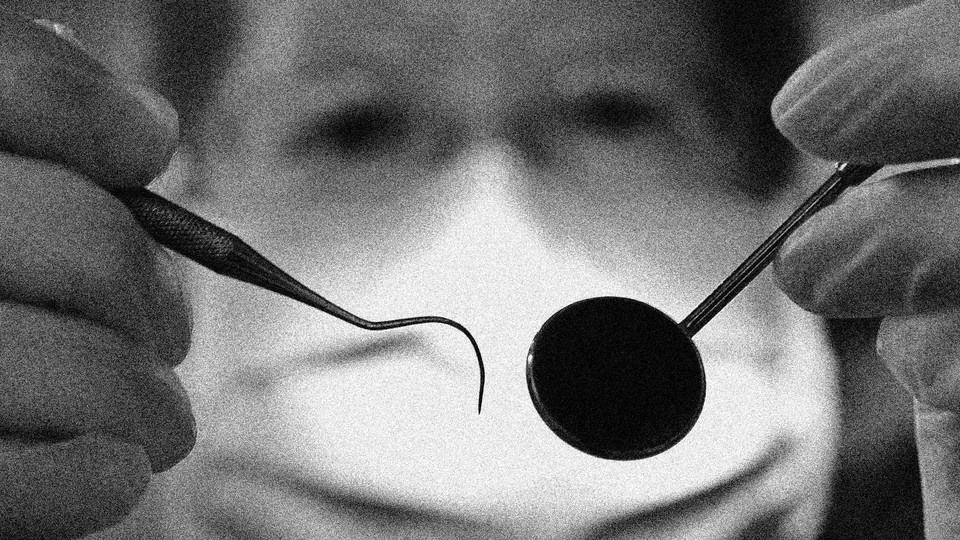 A black-and-white photo of a dentist wearing a face mask and holding up tools