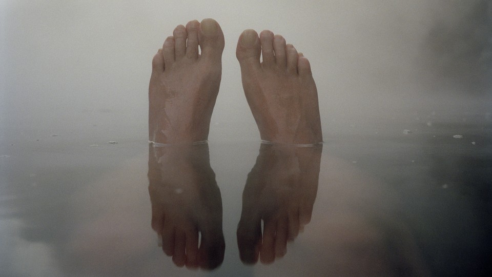 A pair of feet coming out of the water, against a foggy grey sky, and reflected in the water