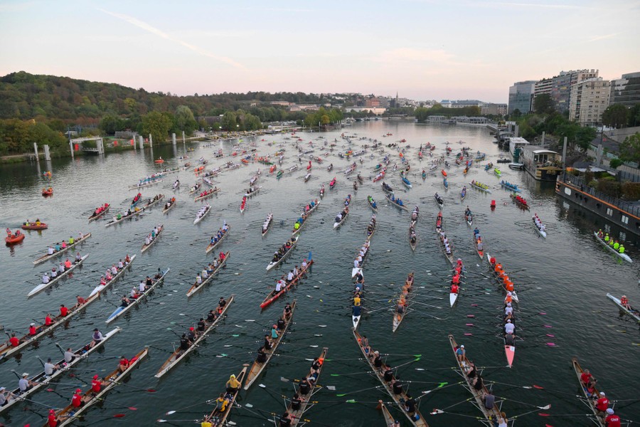 An elevated view of dozens of long rowboats in a river, each rowed by four people
