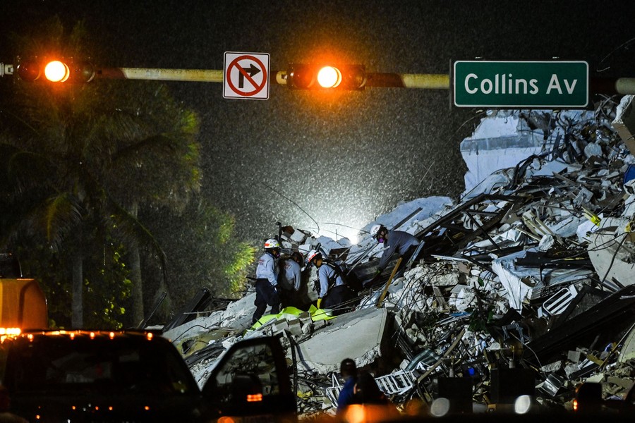 Search-and-rescue personnel work at night, during a brief rainfall, to remove a body from the rubble of a collapsed condominium.
