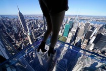 A person stands on a glass-floored platform attached to a skyscraper high above New York City.