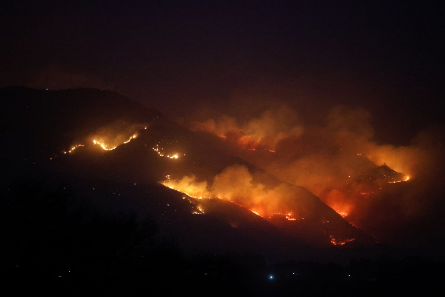 A forest fire spreads across hills, seen at night.
