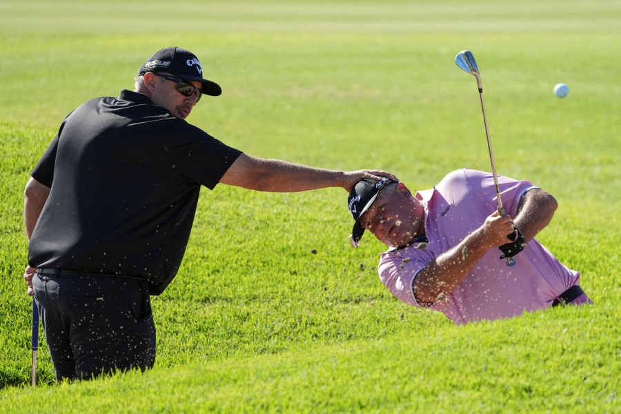 A person reaches out to hold the head of a blind golfer, guiding their shot.