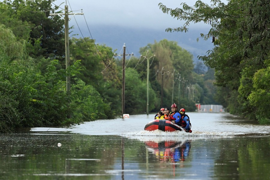 Several rescuers carry people across a flooded area in a small inflatable raft.