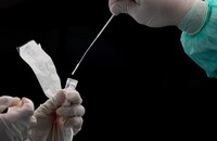 A gloved hand places a nasal swab in liquid to test for COVID-19