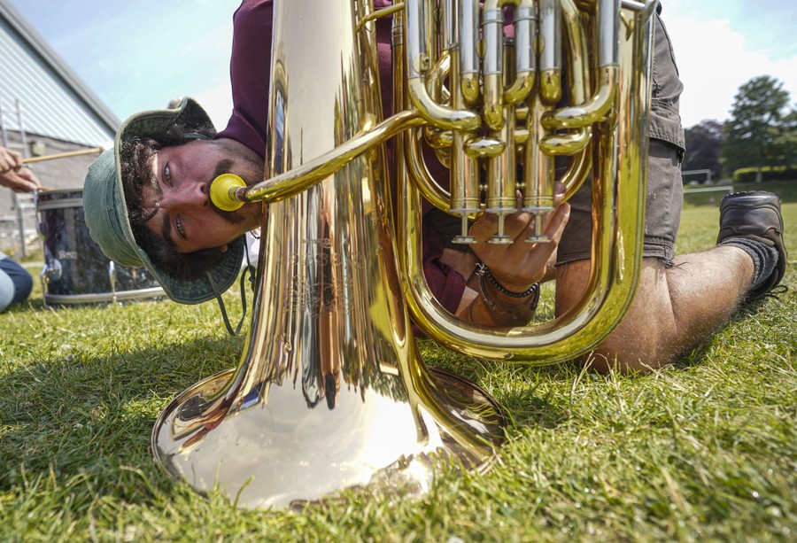 A man blows into a brass instrument with its bell placed the ground.