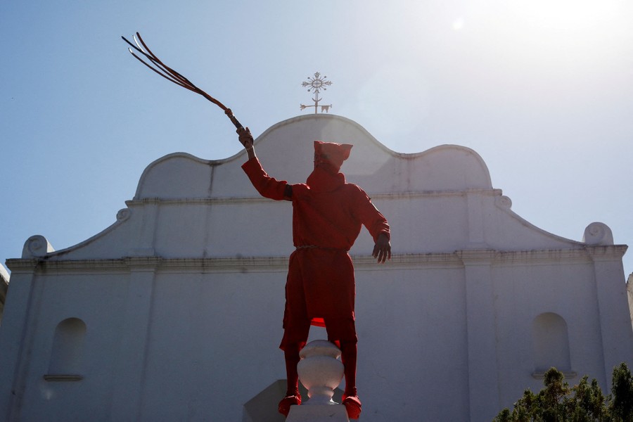 A man dressed as a demon stands on a structure, wielding a whip in an upraised hand.