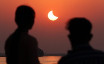 The silhouette of two people watching a partial solar eclipse in a deep-orange sky