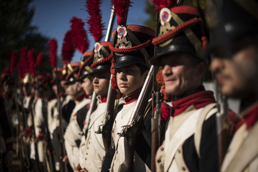 A line of men dressed as Napoleon-era fighters stand at attention.