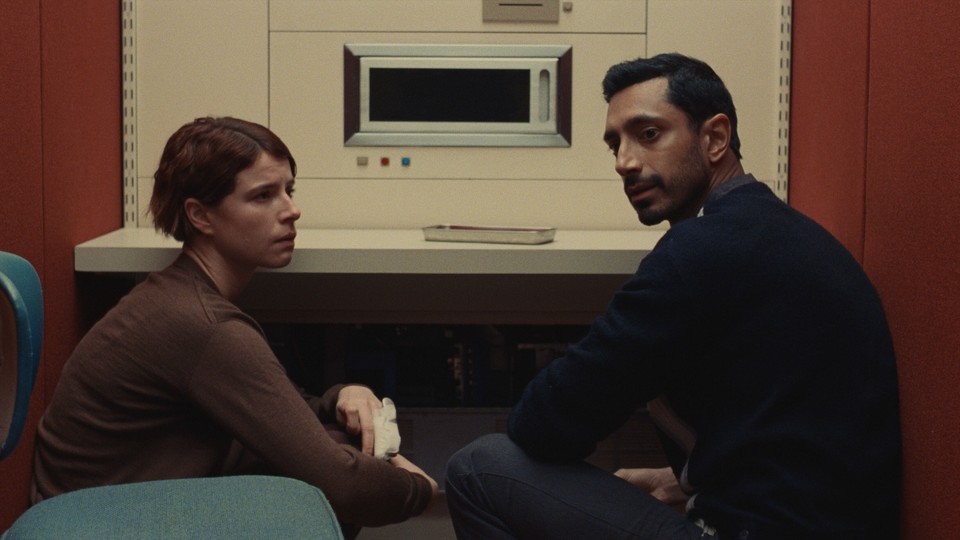 Jessie Buckley and Riz Ahmed sitting together in a retro room