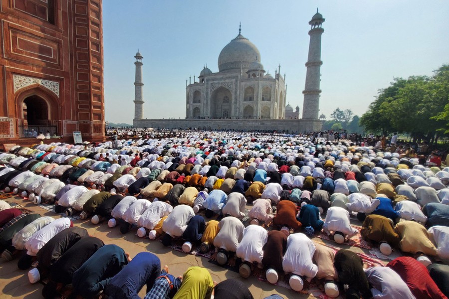 Hundreds of people kneel in prayer in a space in front of the Taj Mahal.