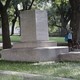 Two passersby take photos of a pedestal where a statue once stood. 