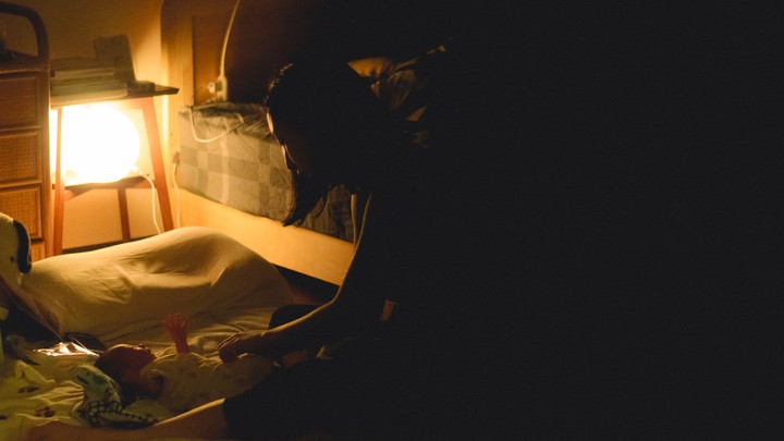 A woman puts a baby to bed in a crib.