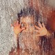 The blurry outline of a parent holding a child with their hands pressed to a glass pane covered in water droplets