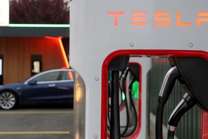 A Tesla Supercharger in the foreground, with a car in the background