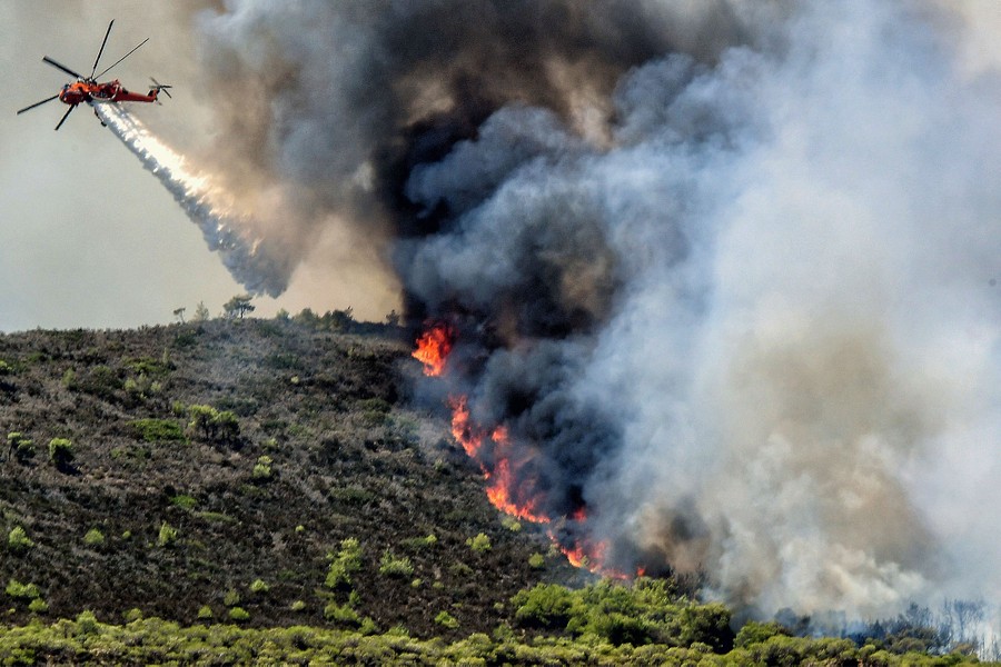 A firefighting helicopter drops water on a wildfire on a hillside.