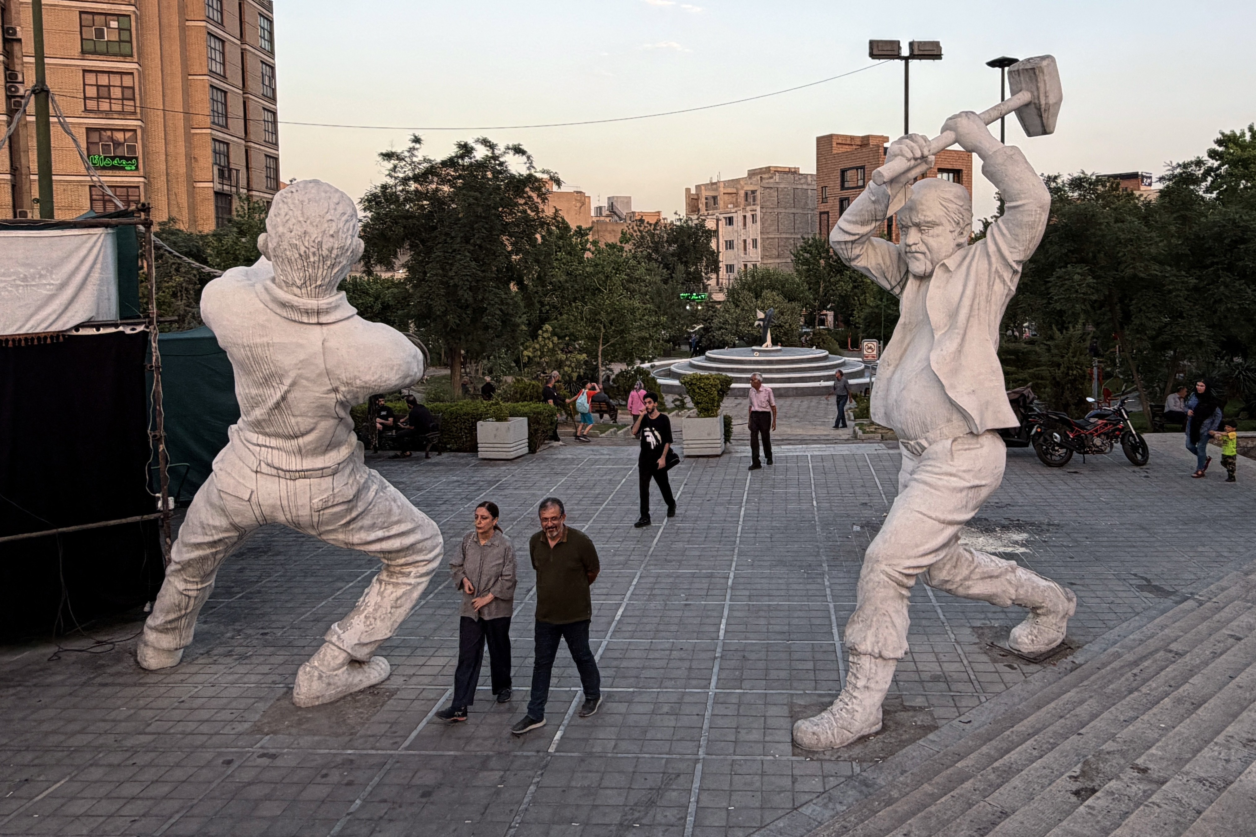 People walk in a square past two tall sculptures of workers.