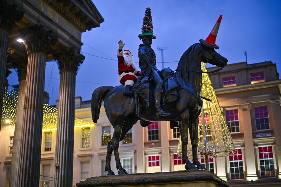 A man dressed in a Santa Claus suit sits atop a large statue of a horse and rider.