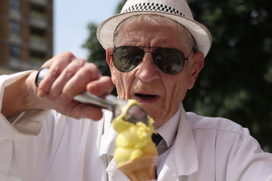 An ice cream vendor uses a scoop to place ice cream in a cone.