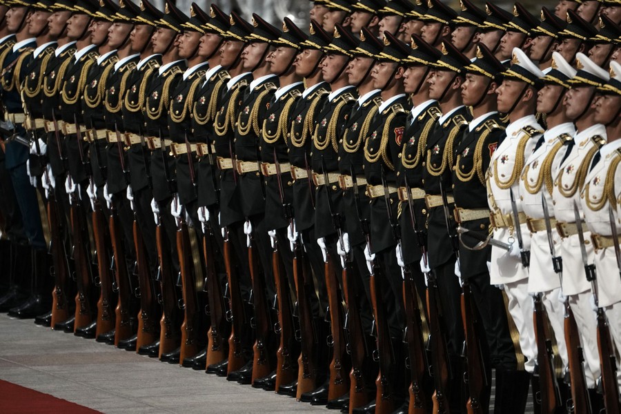 Soldiers in dress uniforms stand at attention in neat rows.