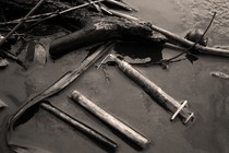 Black-and-white photo of a syringe among other debris that's been washed up on a beach
