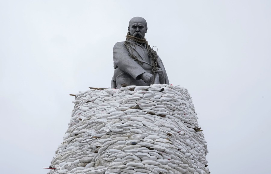 A tall statue stands partially covered by sandbags.